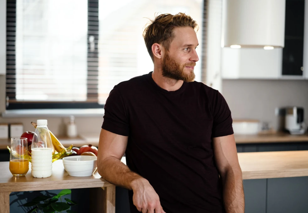 En enslig ung, kjekk mann som står på kjøkkenet sitt og ser ut i luften