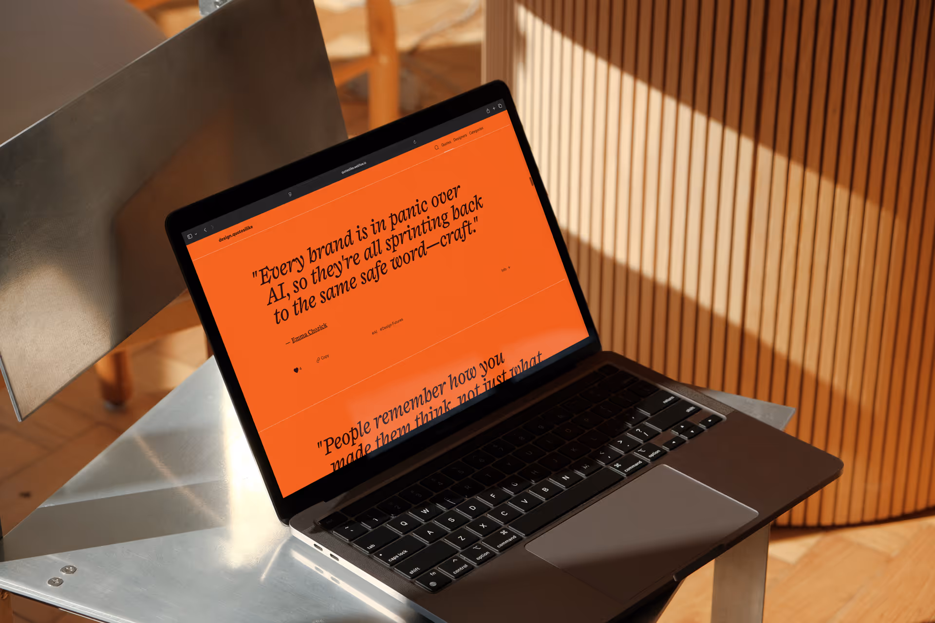 Laptop on metal chair displaying the Design Quotes I Like website on an orange background.