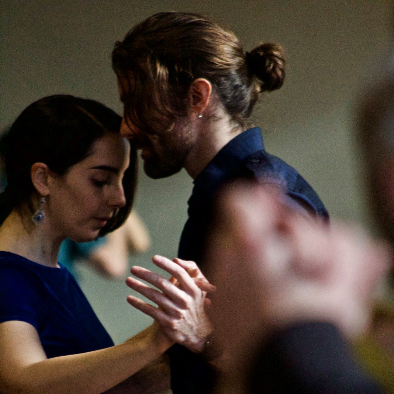 Photograph of Tye Newton—a man with long hair tied back, wearing a blue button-up shirt—framed from elbows up, embracing with a dance partner.