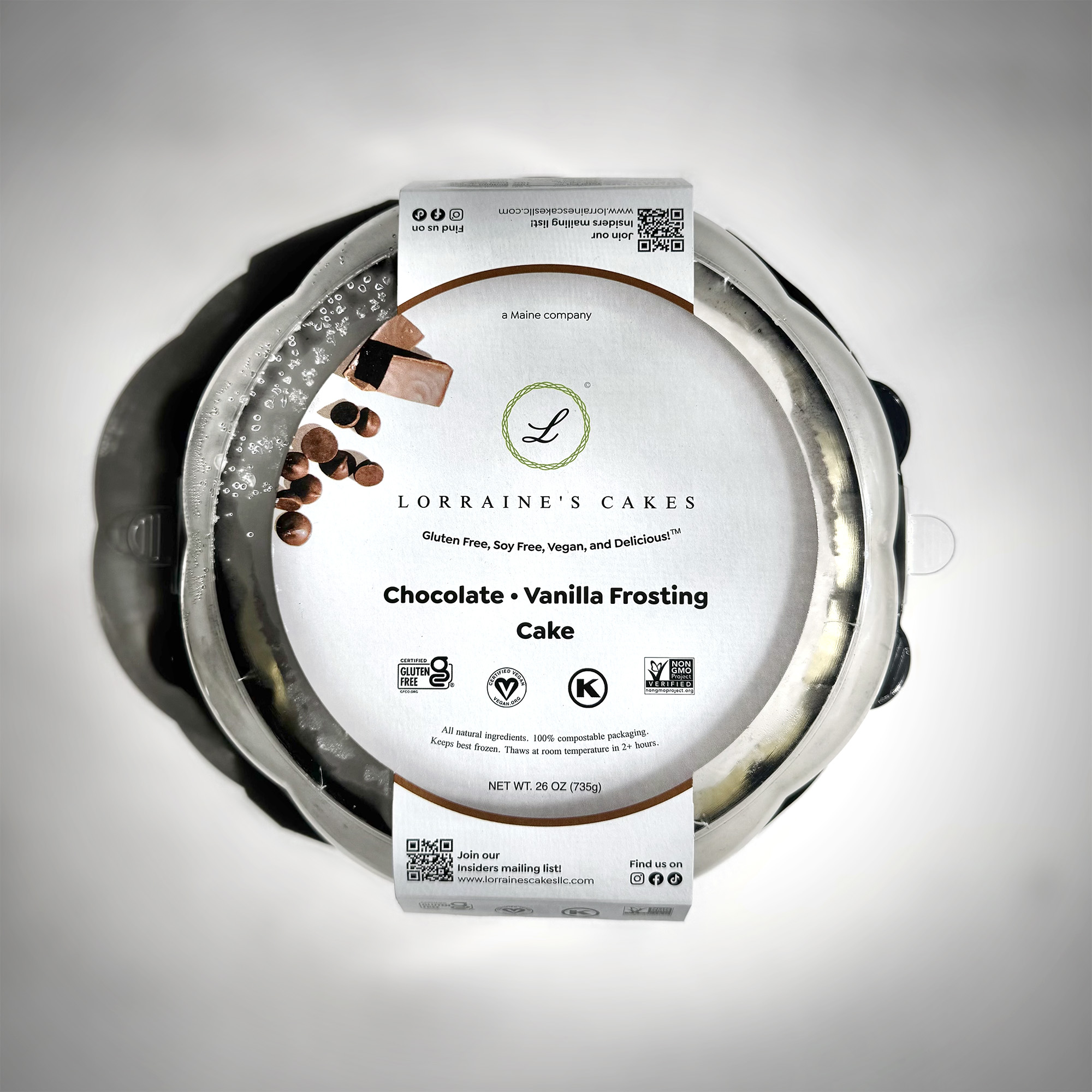A top-down view of a Lorraine's Cakes chocolate cake in its package: a thick card-stock sleeve printed with branded graphics around a clear, compostable plastic dome.