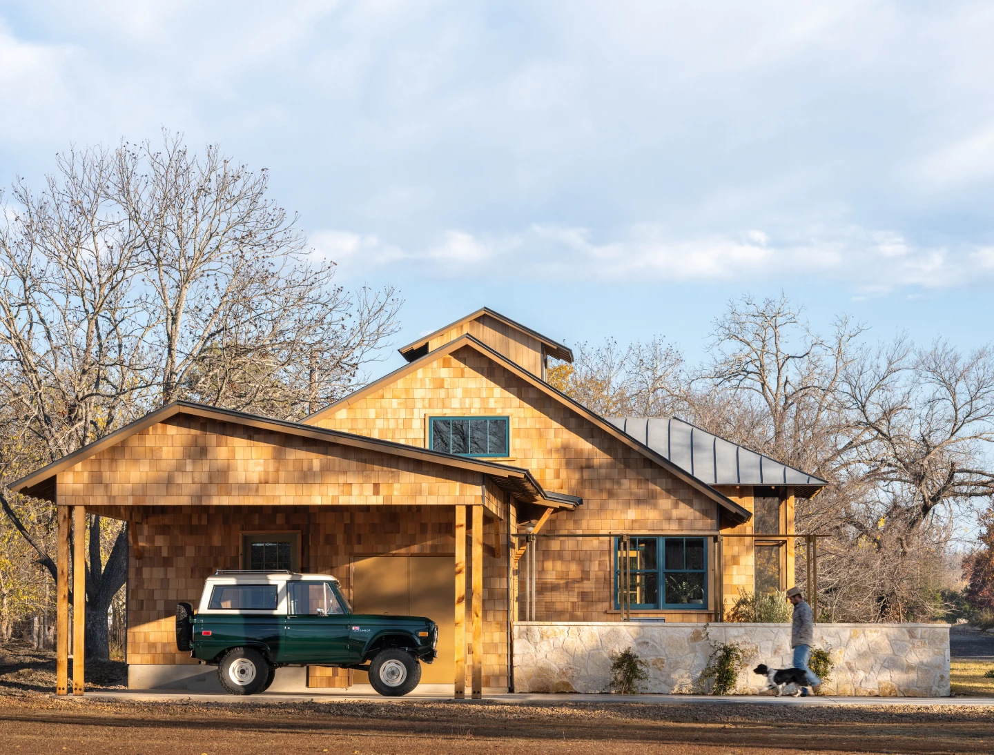 Camp Bluebird home exterior from side, SUV in driveway and man and dog walking