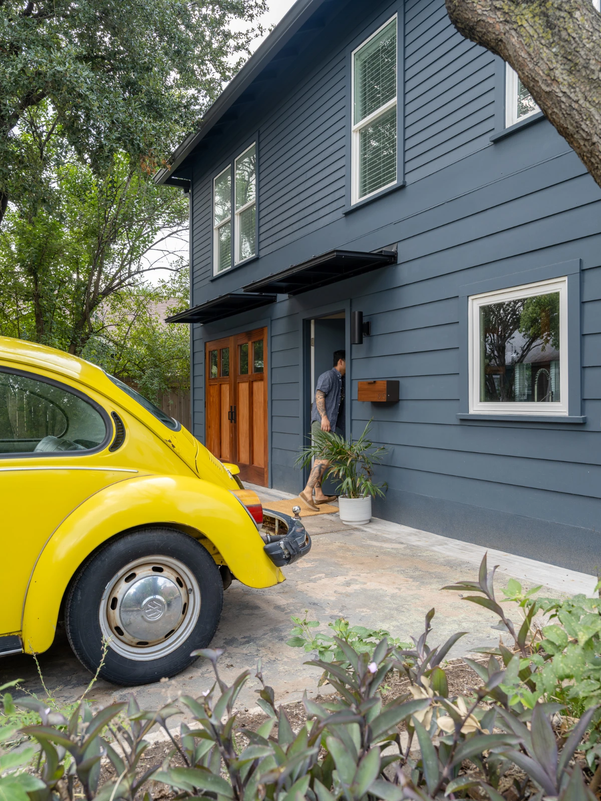 The Carriage House exterior, showing dark siding accented with warm wood garage doors and a bright yellow VW beetle