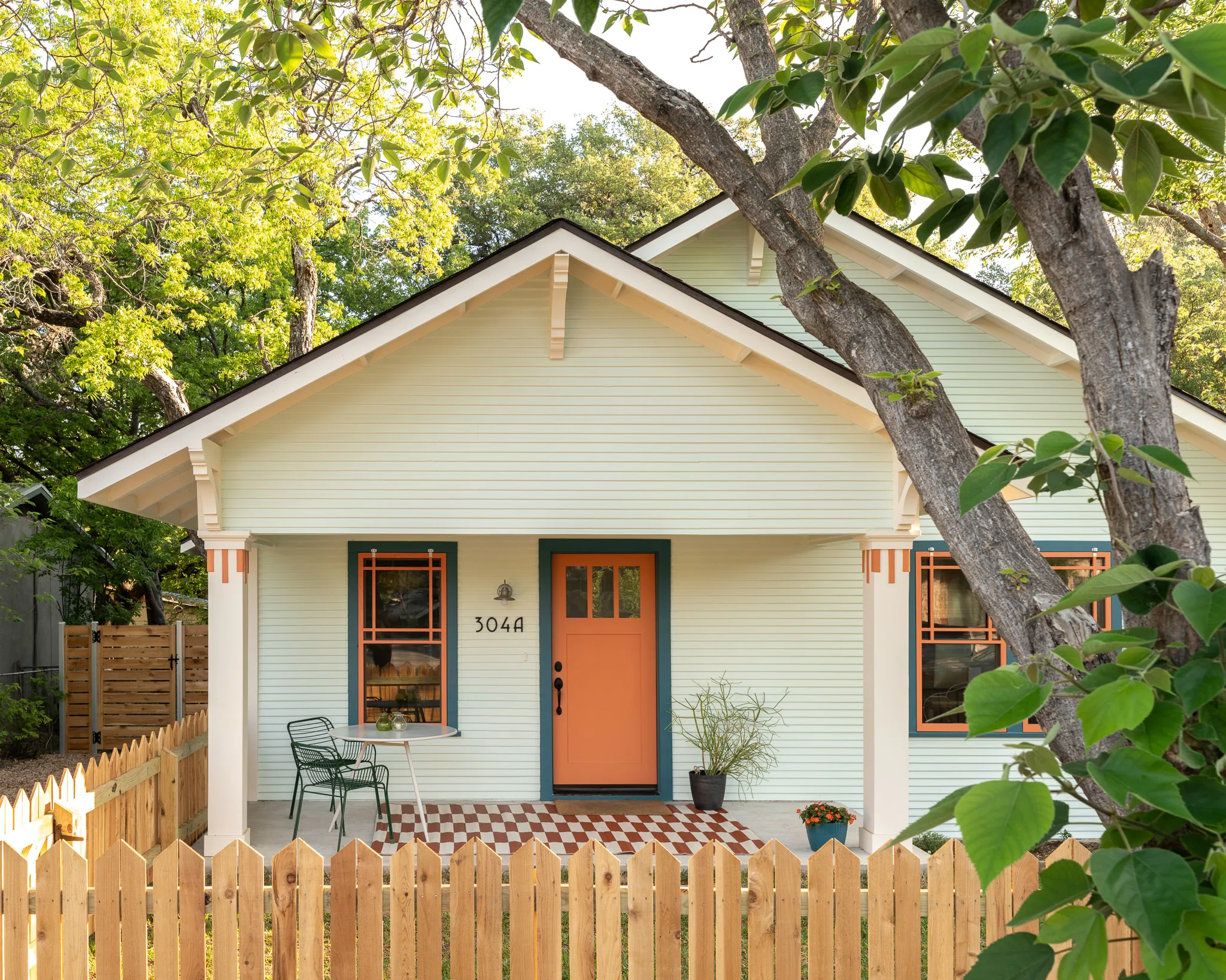 Front exterior of the SOCO Duo home, showing pale green siding accented by orange craftsman details and ringed by a picket fence