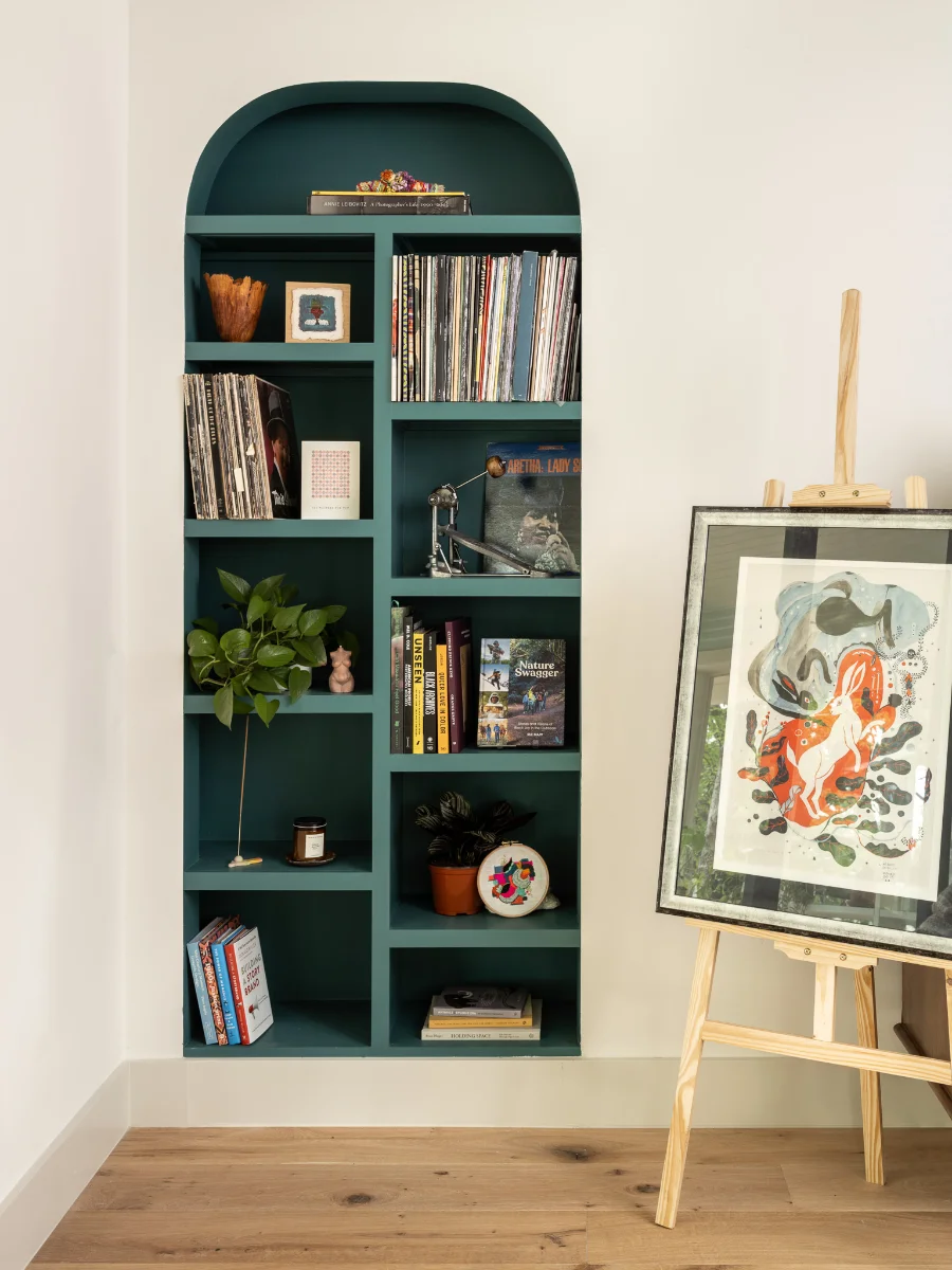 A corner of the SOCO Duo home with a teal arched built-in bookshelf and a piece of art sitting on an easel