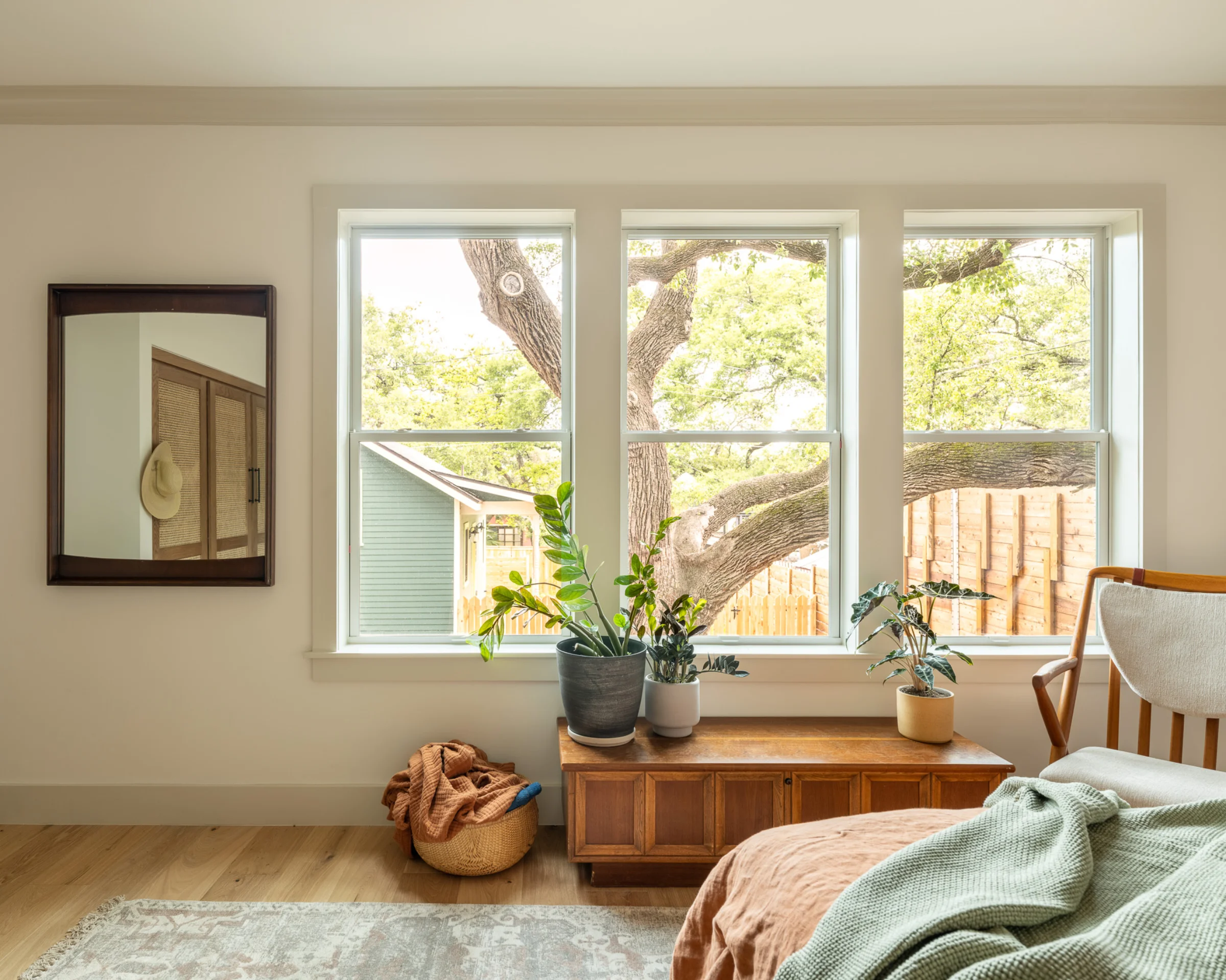 A bedroom in SOCO Duo, with a large set of three windows, some plants on a credenza, and a rumpled, cozy bed