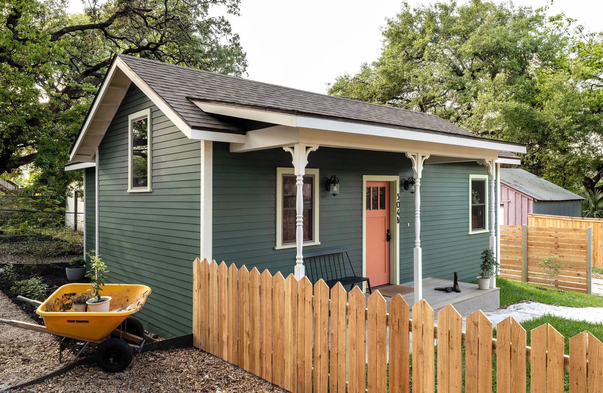 A side view of The Backhouse, a dark green cottage with wood fencing and a lush grass yard