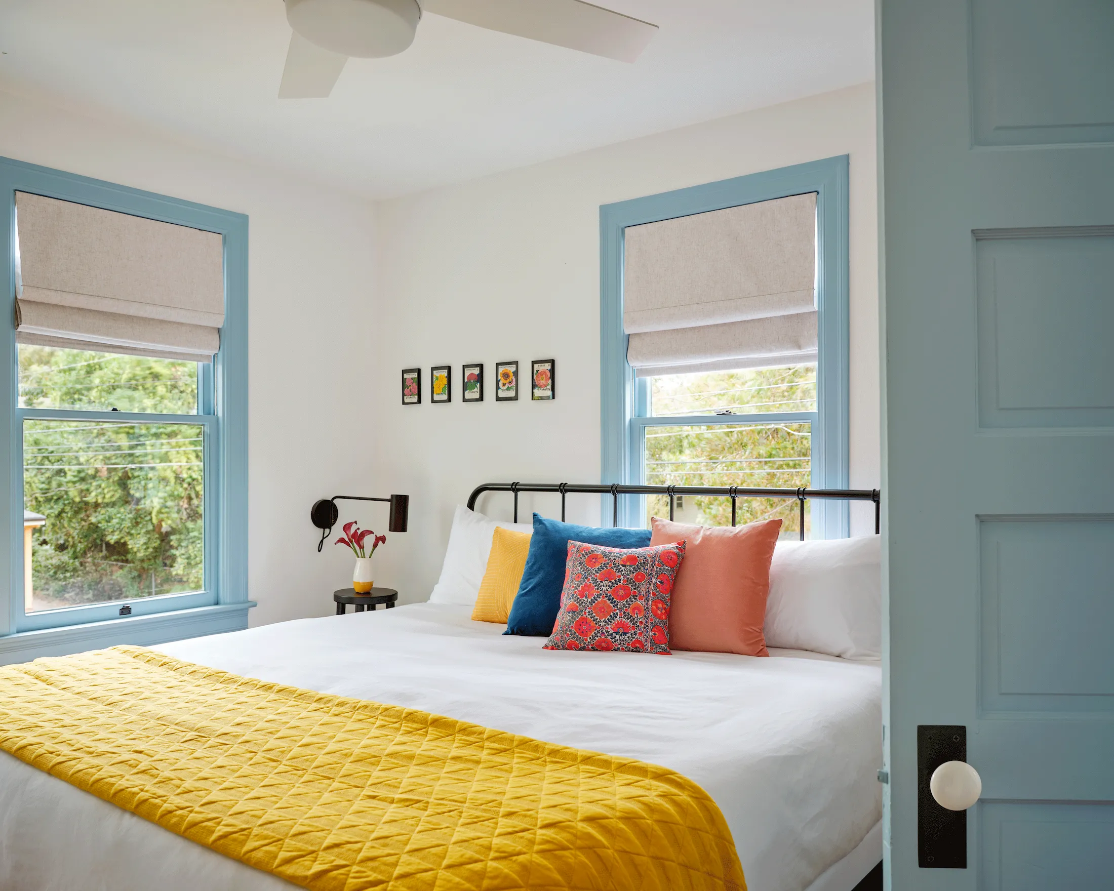 A view of a bedroom in Guesthouse East. The central bed is set with clean white bedding and accented with primary-colored pillows.