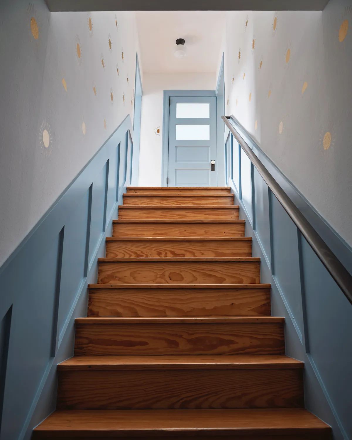 A stairwell in Guesthouse East. The walls feature light blue wainscot combined with white walls scattered with gold sun motifs.