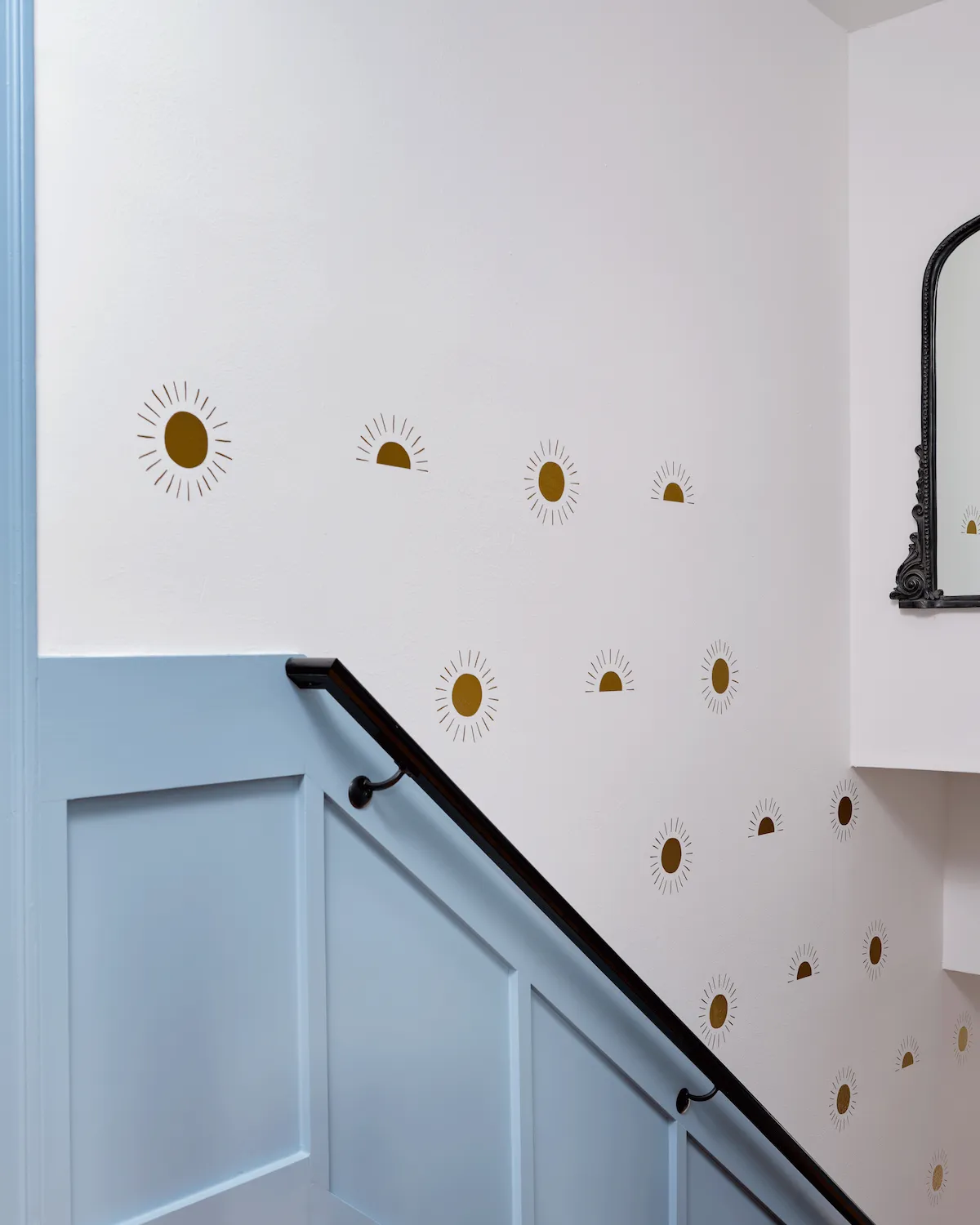 An alternate angle of the Guesthouse East stairway. The walls feature light blue wainscot combined with white walls scattered with gold sun motifs.