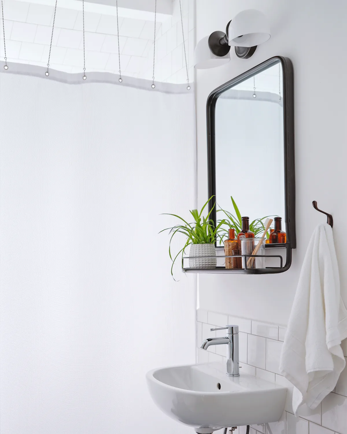 A bathroom in Guesthouse East is decorated with white tile on white walls. A modern black-rimmed mirror accents the wall.