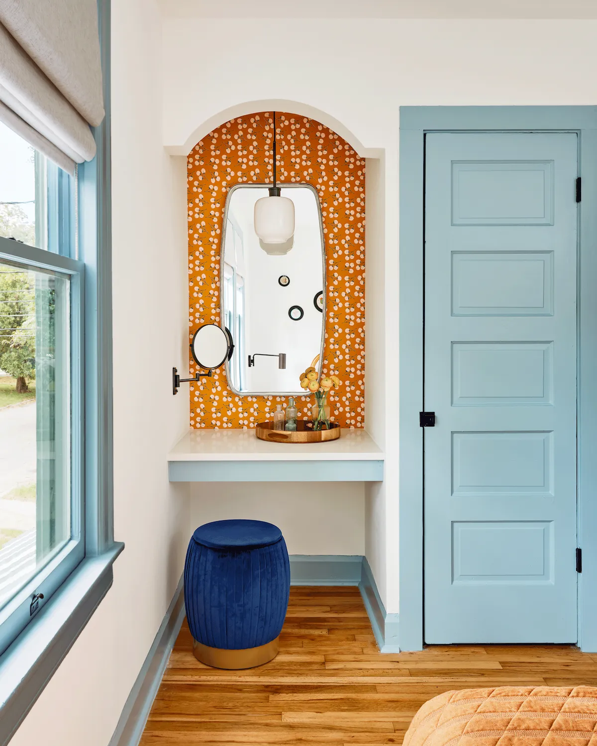 A built-in, orange-wallpapered vanity in Guesthouse East is framed by white walls and light blue woodwork. 