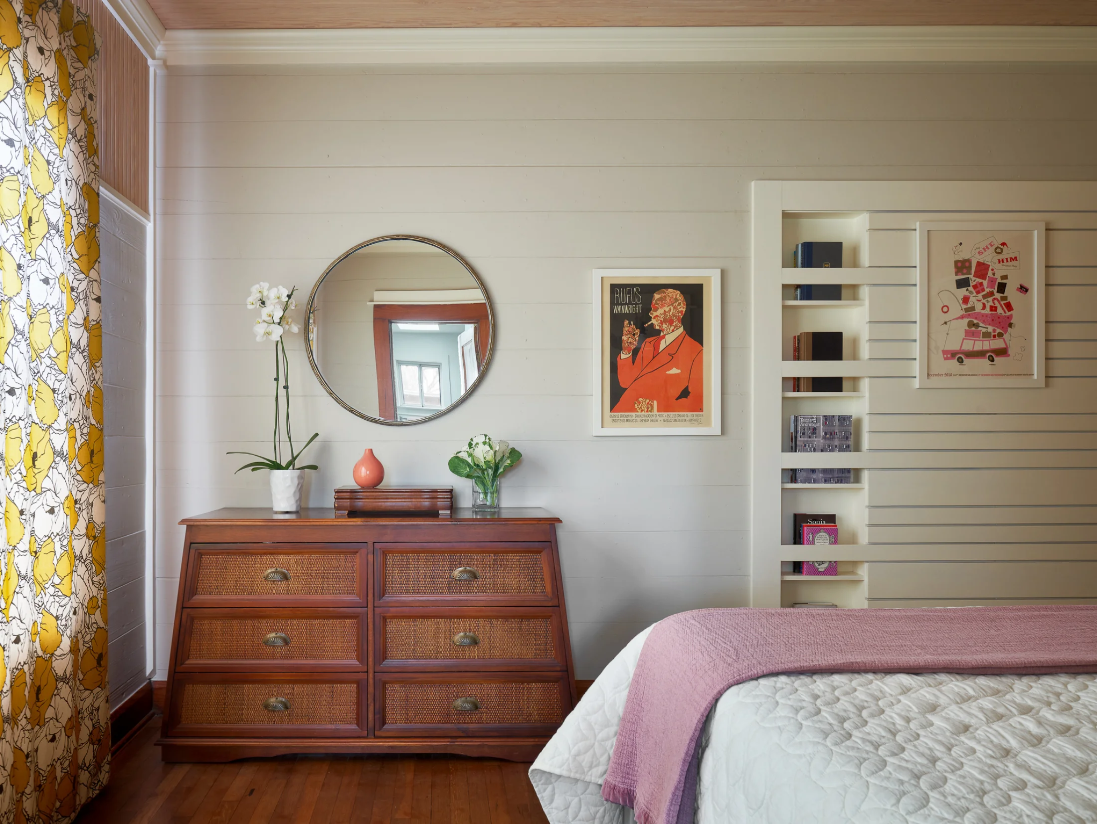 An alternate view of a Wende Bungalow bedroom. An antique dresser holds a pot of white orchids underneath a modern round wall mirror.