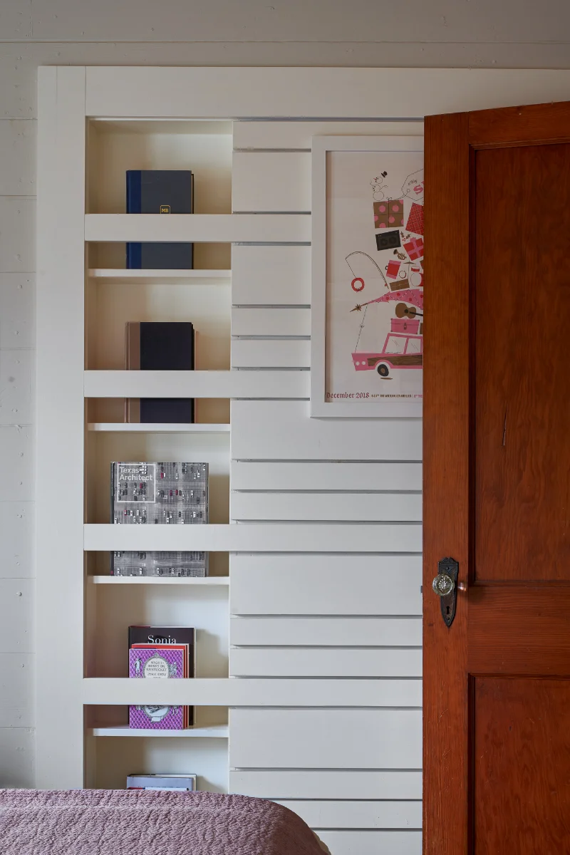 In a Wende Bungalow bedroom, a built-in shelving unit holds a handful of books. 