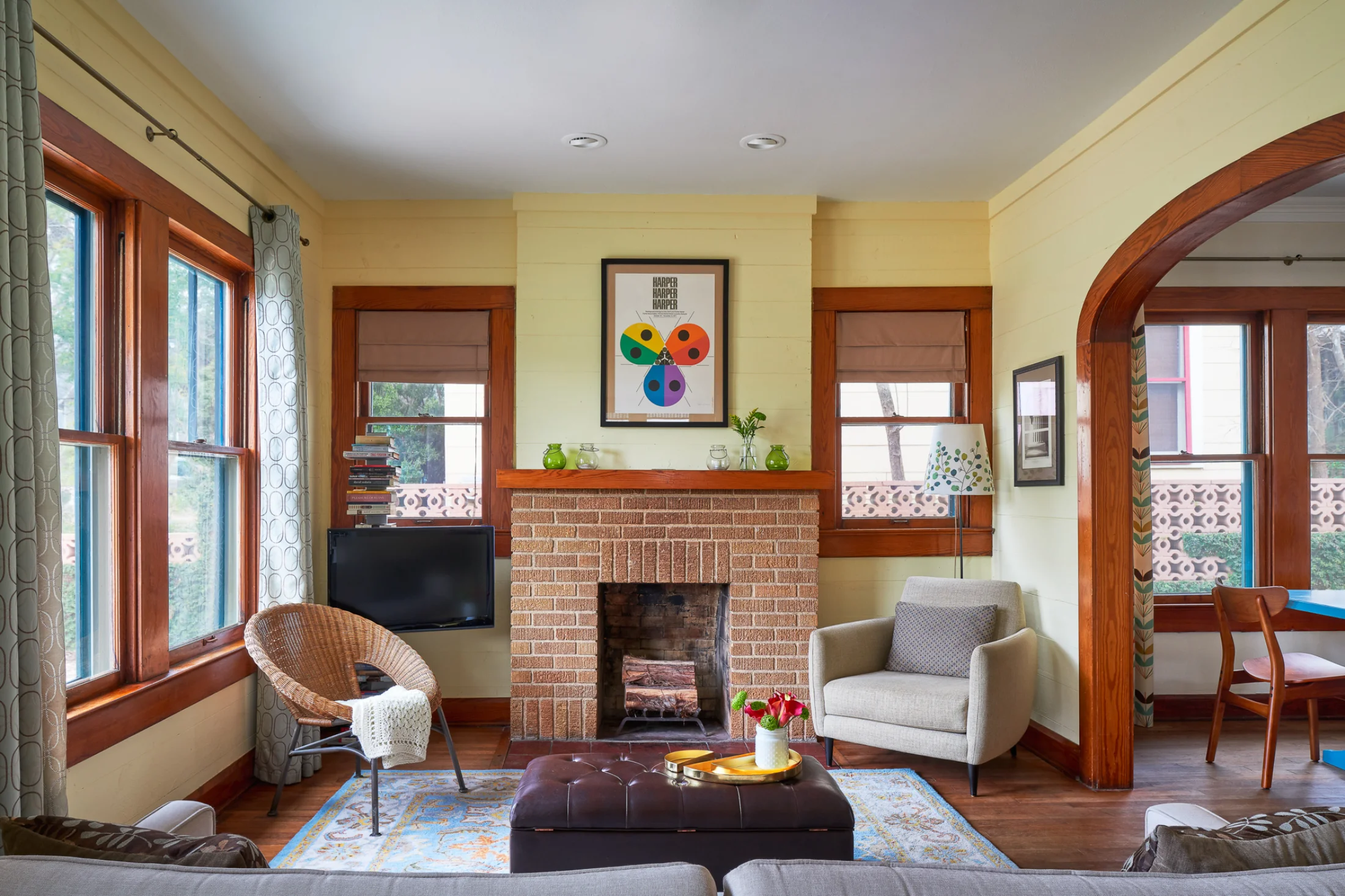 The living room of Wende Bungalow is arranged around a central brick fireplace. Craftsman-style woodworking frames yellow-paneled walls.