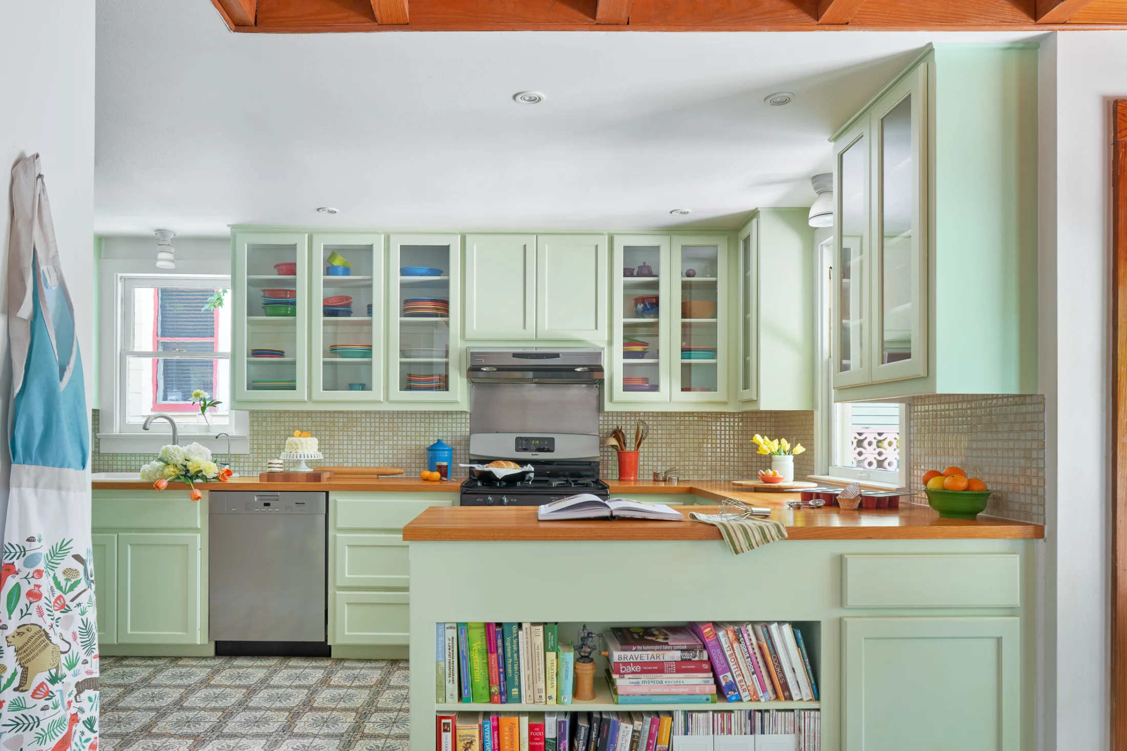 An alternate view of the Wende Bungalow kitchen frames a large, well-appointed space. Colorful books and dishes accent the pale green cabinetry.
