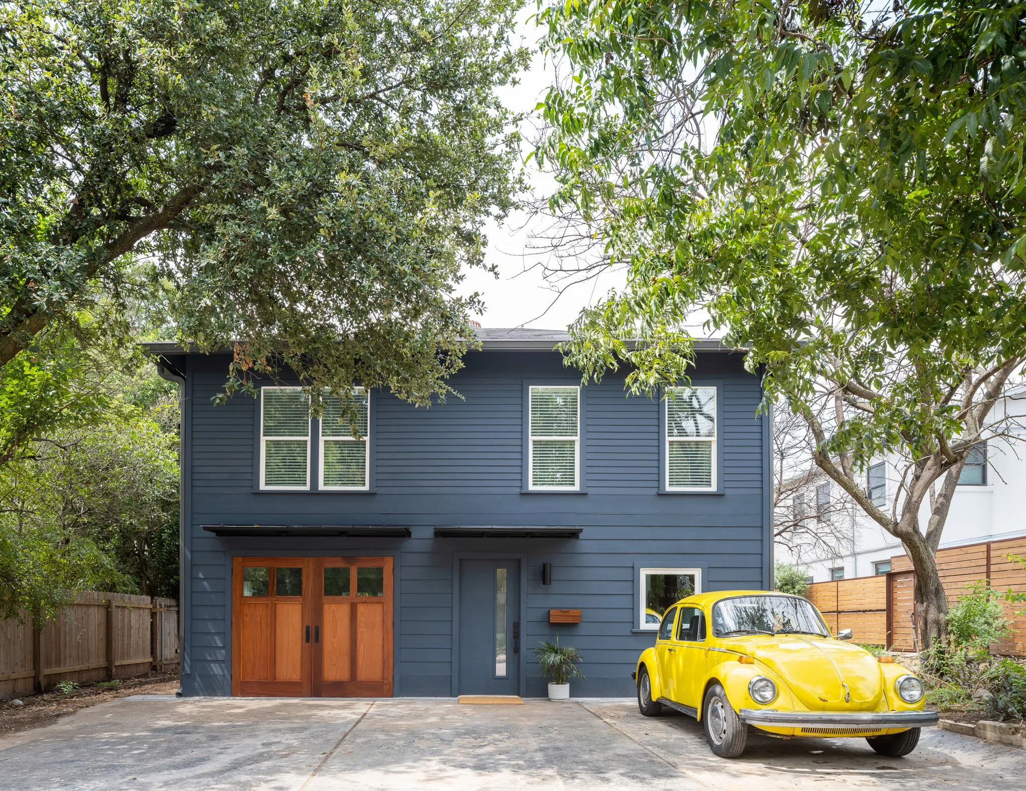 The front of the Carriage House is adorned with navy siding and warm wood garage doors. A yellow vintage VW beetle sits in the driveway.