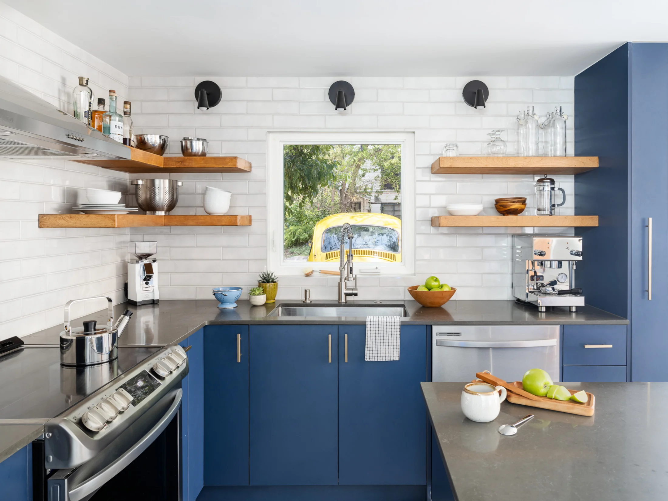 The Carriage House kitchen feels clean and modern with navy blue cabinets, wood upper shelves, and white subway tiled walls.