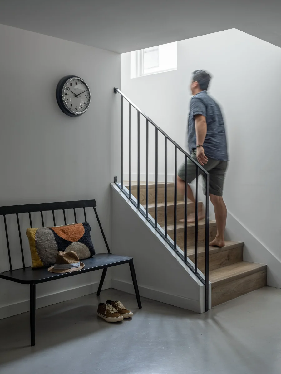 A man ascends a modern stairway in the Carriage House. The hall is decorated with a black bench and vintage wall clock.