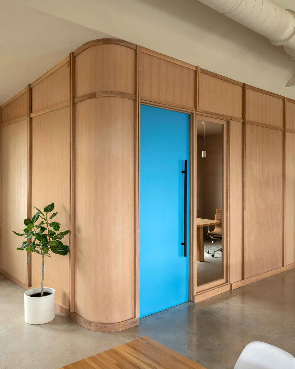 A corner view of a private office space in the FBG Office. Wall-to-ceiling wood paneling frames a bright blue door. 