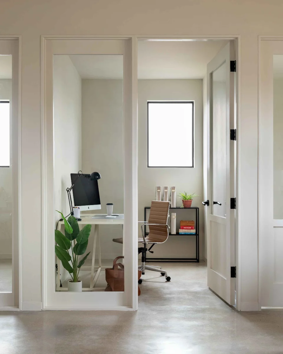 A doorway in the FBG Office frames a private room furnished with a modern desk, chair, iMac, and healthy houseplants.