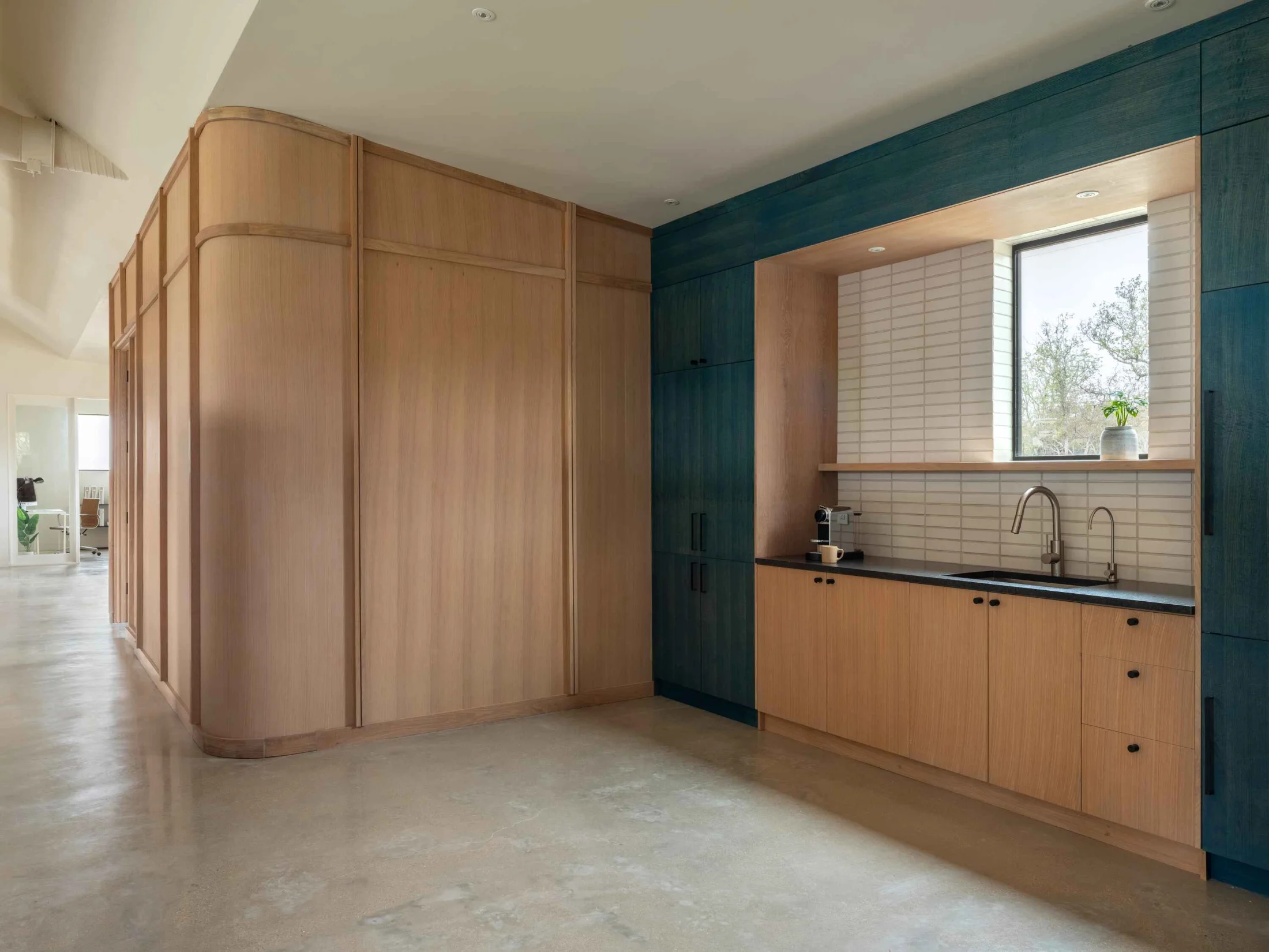 A FBG Office common space is furnished with an efficiency kitchen. Dark green and wood cabinetry frames a generous counter space.