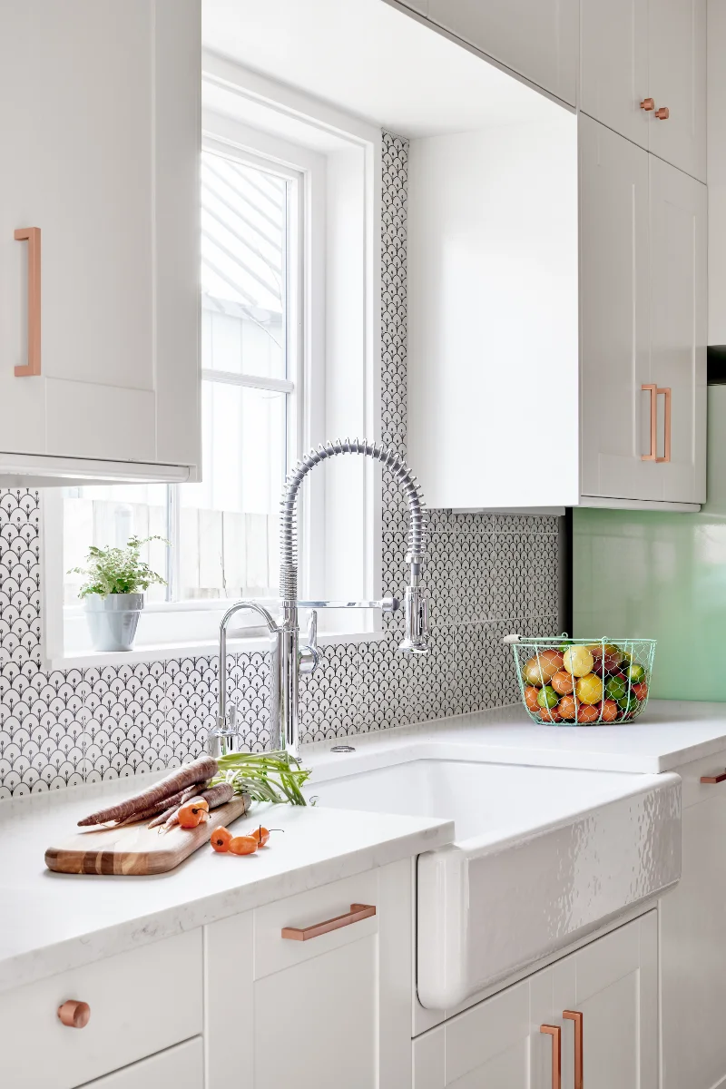 An alternate view of the Queen Anne House kitchen showcases the white farmers sink and chrome faucet fixtures. Some vegetables sit on the counter.