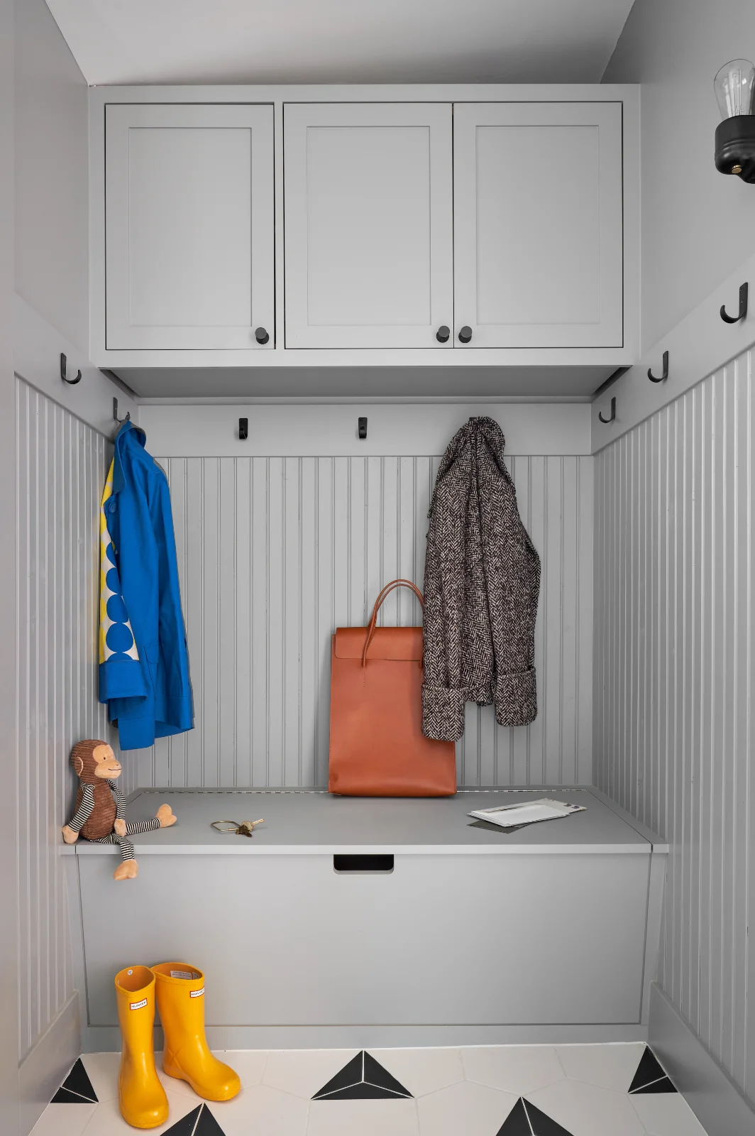 A corner in the Queen Anne House is furnished with mudroom-styled built-ins. Coats hang on the wall, and yellow Hunter boots sit on the floor.