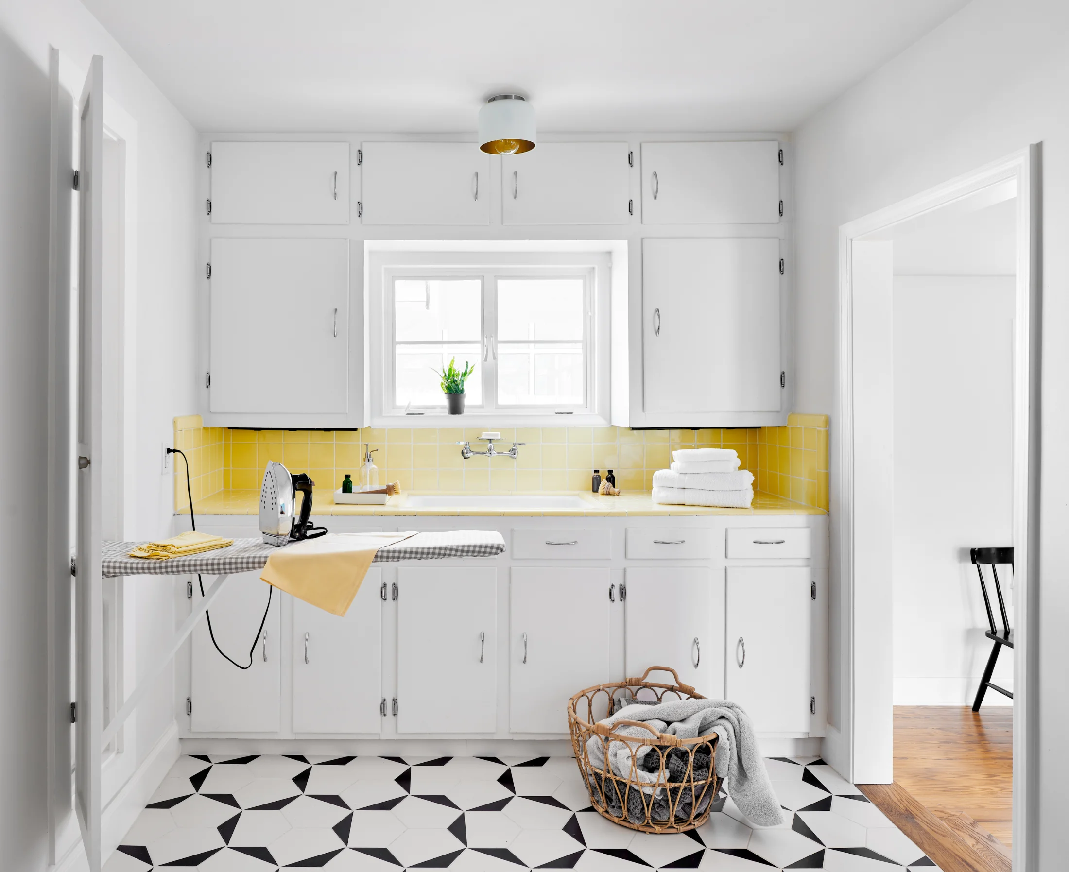 A laundry space with cabinetry and a swing-down ironing board in the Queen Anne House. White cabinets are framed with sun yellow tile.