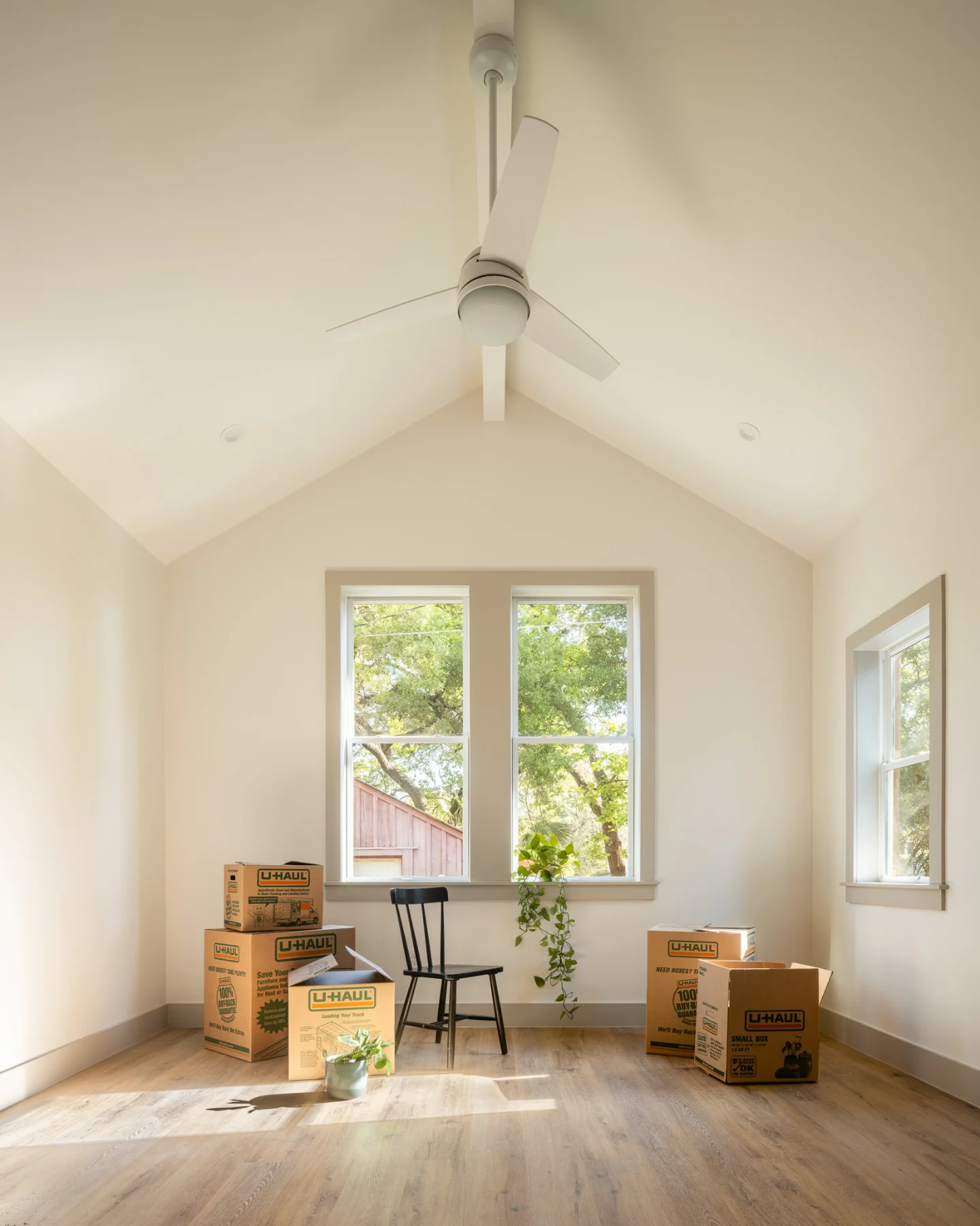 A room in the Back House showcases a vaulted ceiling, creamy walls, and wide wood flooring. The room is empty aside from some U-Haul boxes.