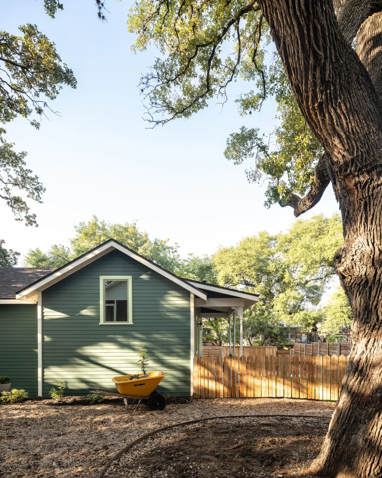 A side view of the Back House. In the foreground, a garden space with a yellow wheelbarrow.