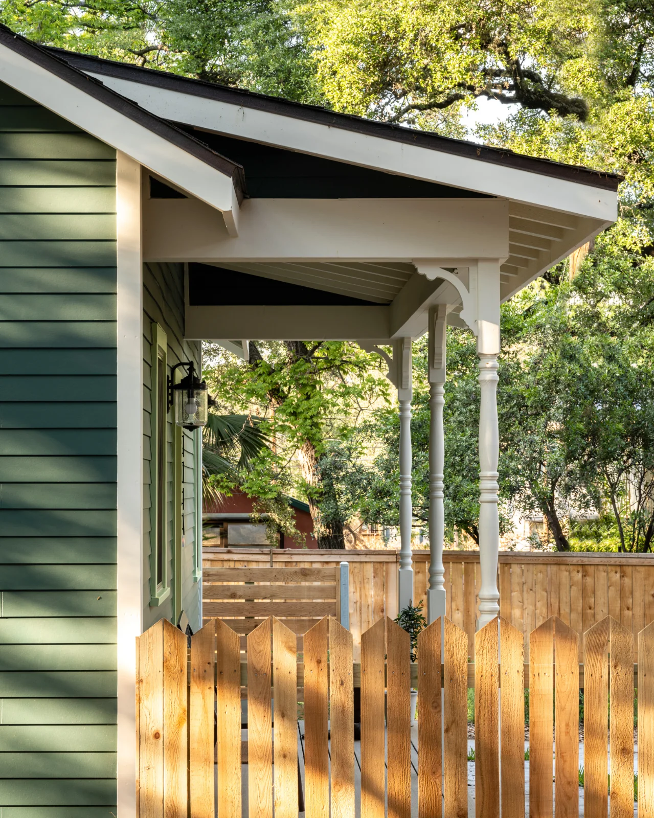 A side closeup of the Back House shows the combination of green siding, white woodwork, and wood picket fencing.