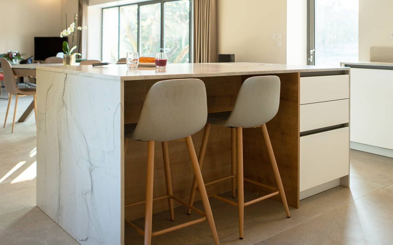 Projet de l'Atelier de Léa : focus sur l'îlot central en marbre d'une cuisine contemporaine minimaliste blanche sur-mesure.