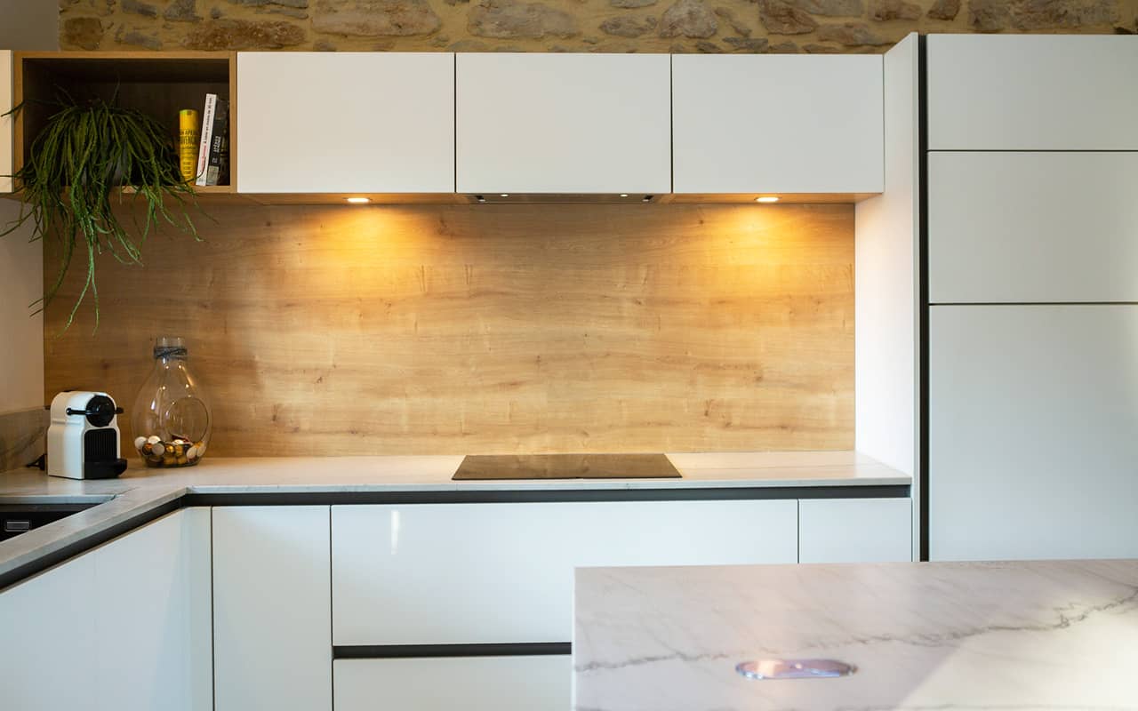 Projet de l'Atelier de Léa : focus sur les placards, la façade en bois et le plan de travail marbre d'une cuisine contemporaine minimaliste blanche sur-mesure.