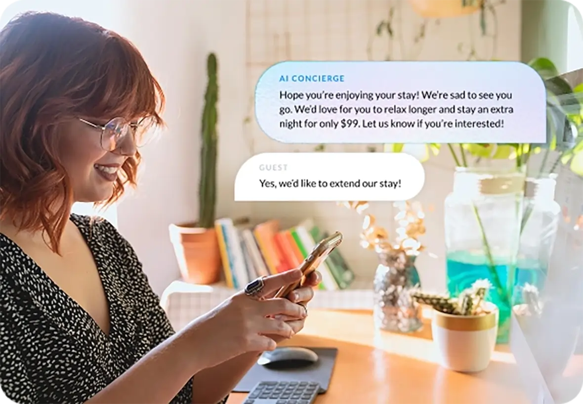 Smiling woman with glasses using a smartphone at a desk, with chat bubbles showing a conversation about extending a hotel stay.