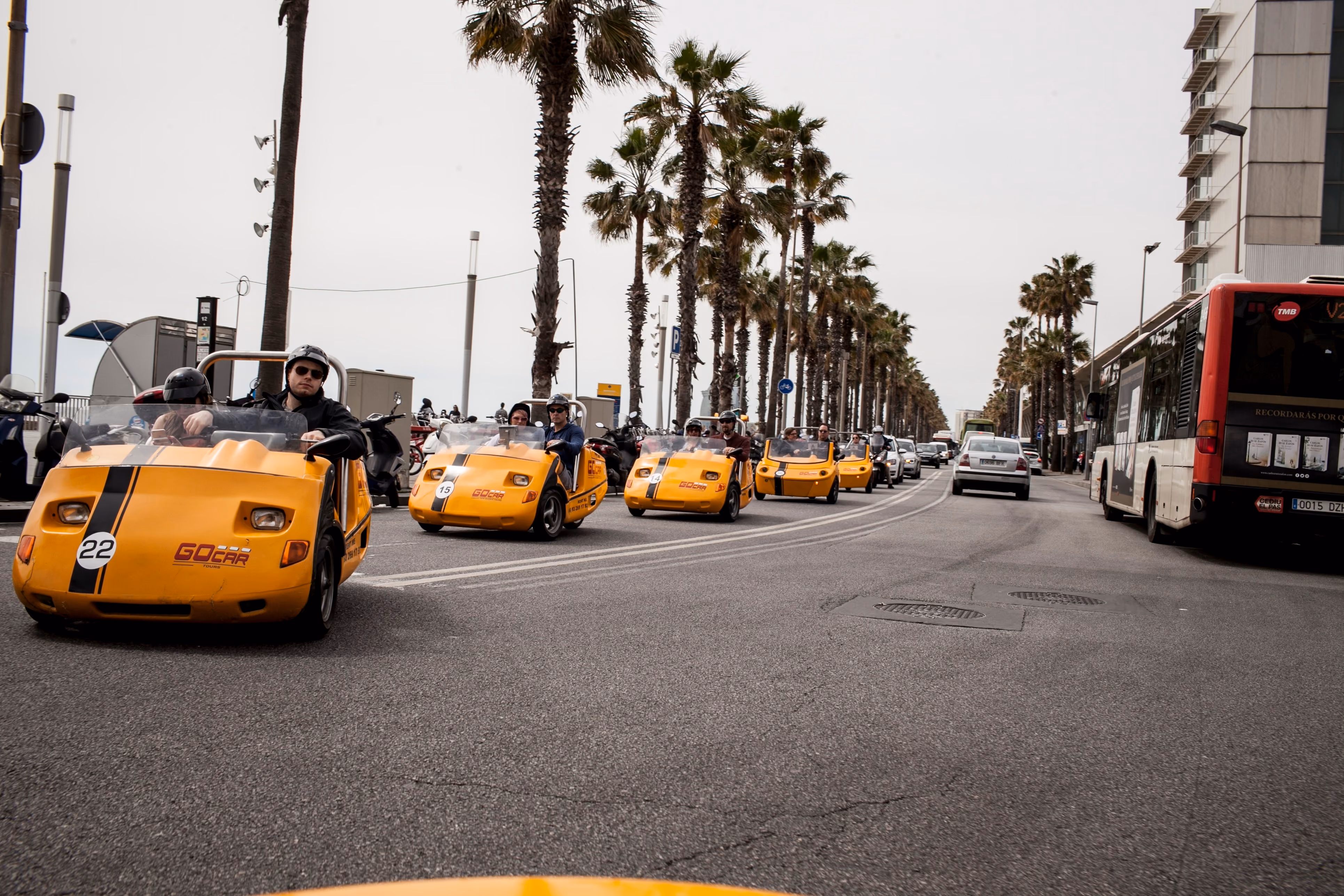 Yellow GoCar tour vehicles driving along palm-lined street in city