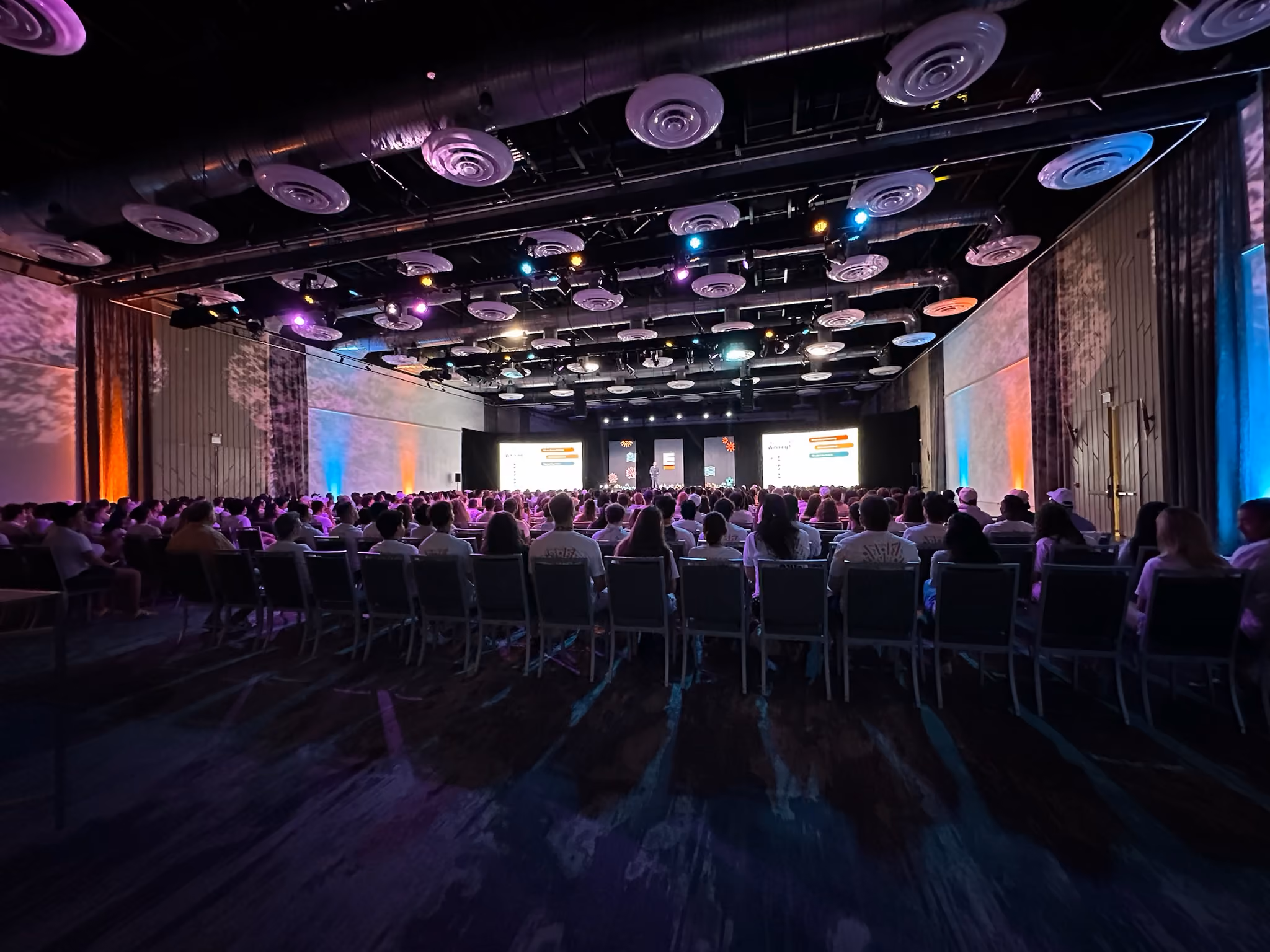 Crowded conference room with colorful lighting and presentation screens