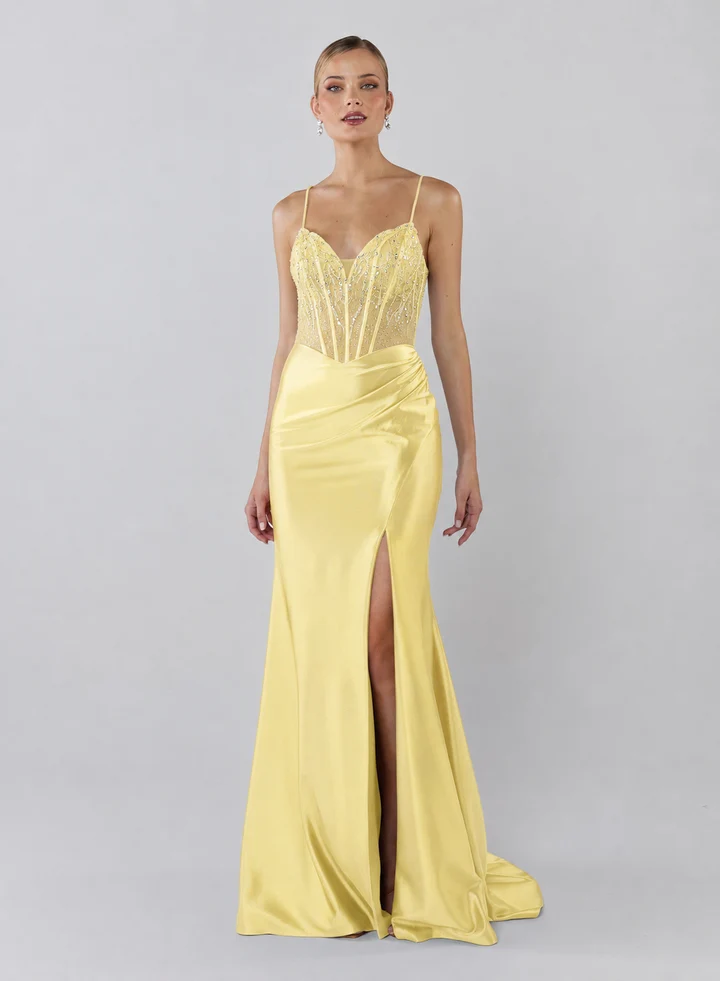 The Carmella Formal Dress is a fitted, full-length gown crafted from stretch satin for a sleek, contoured silhouette. The skirt features a thigh-high split and ruching from one hip, adding movement and flattering definition.