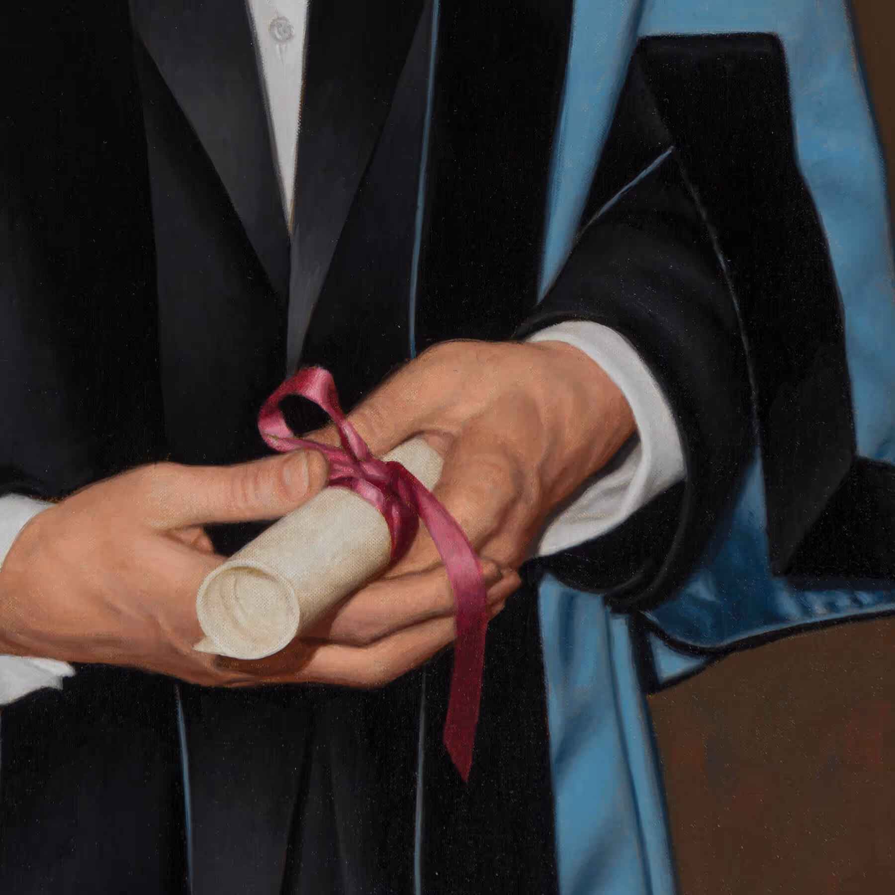 Detail of Edward Cripps holding a diploma tied with a ribbon while wearing academic regalia.