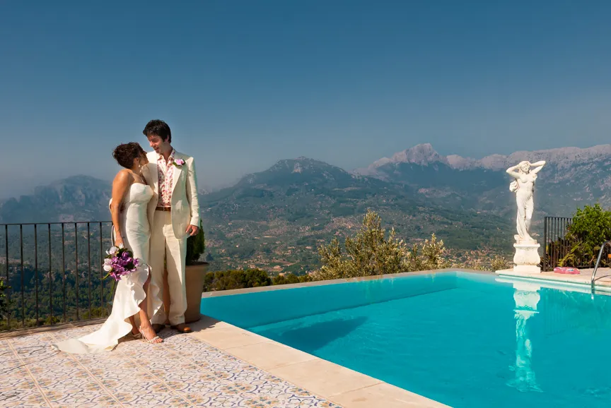 Bride and groom standing by a pool with mountain landscape in the background.