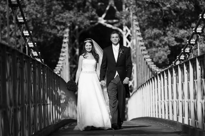 Bride and groom holding hands walking on a bridge during their wedding.