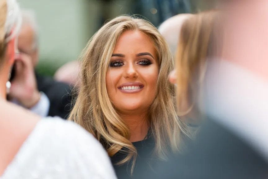 Smiling blonde woman with styled hair and makeup in a crowd.