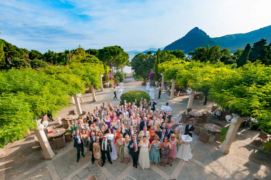 Large group of people posing for a photo at an outdoor event in a garden area with trees and mountains in the background.