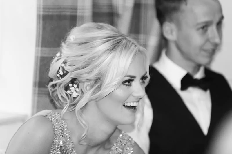 Smiling blonde woman with an elegant updo hairstyle and beaded dress, next to a man in a bow tie and vest.