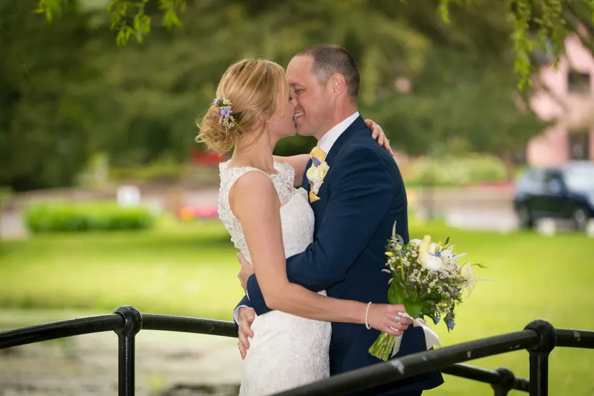 Bride and groom embracing closely on an outdoor bridge with greenery in the background.