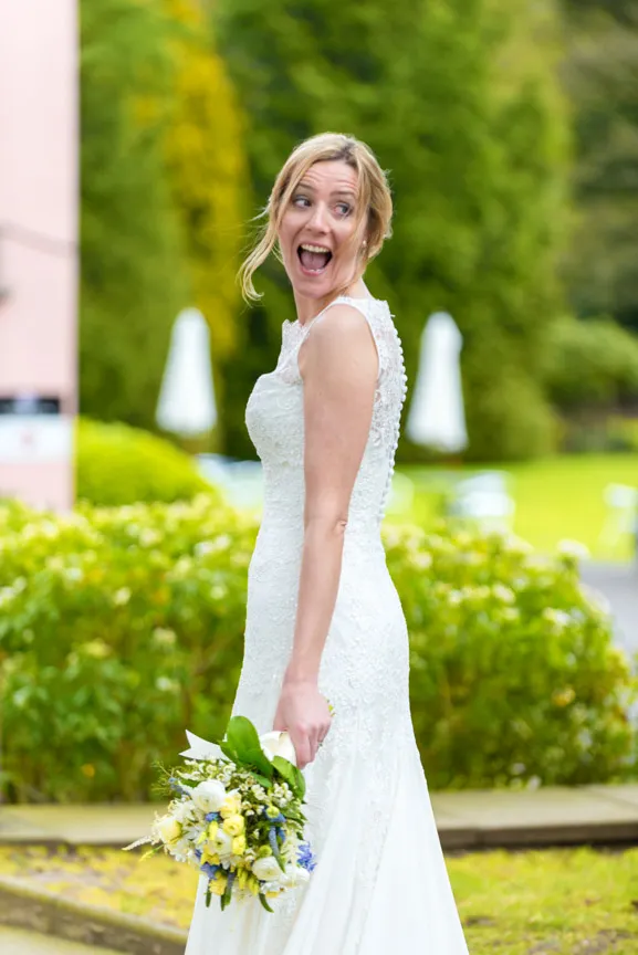 Happy bride in a lace wedding dress holding a bouquet of white and yellow flowers outdoors.