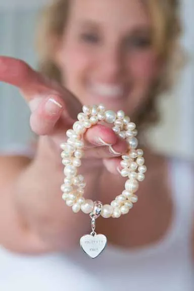 Hand holding a pearl bracelet with a heart-shaped charm that reads 'MOTHER'S DAY'.