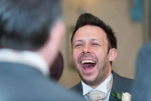 Man in a suit laughing happily at a social event, facing another person.