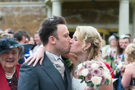 Bride and groom kissing during outdoor wedding ceremony with guests in background.