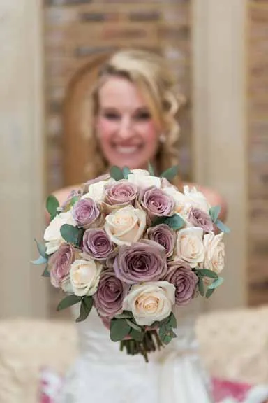 Bride holding a bouquet of pale pink and cream roses with green leaves.