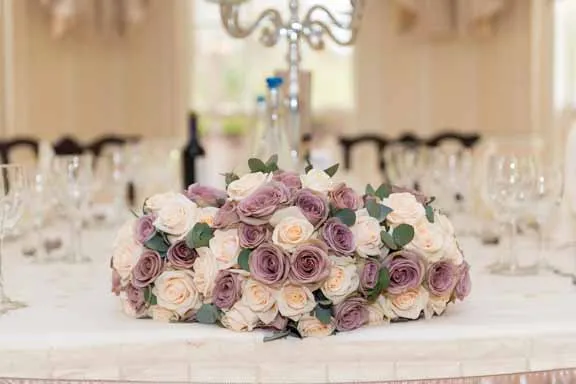 Bouquet of cream and lavender roses with green leaves on a white tablecloth at a formal dining table.
